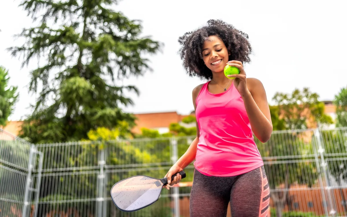 happy woman serving pickelball in an outdoor court utc
