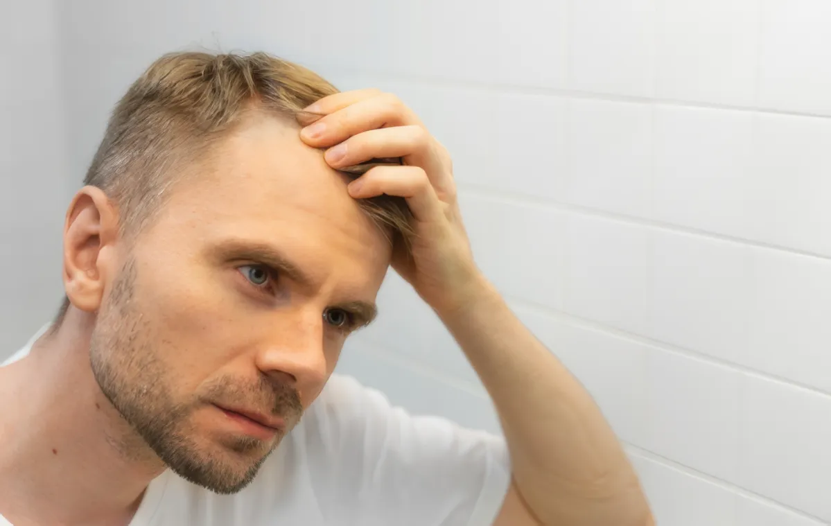 man examining hairline in mirror at home utc