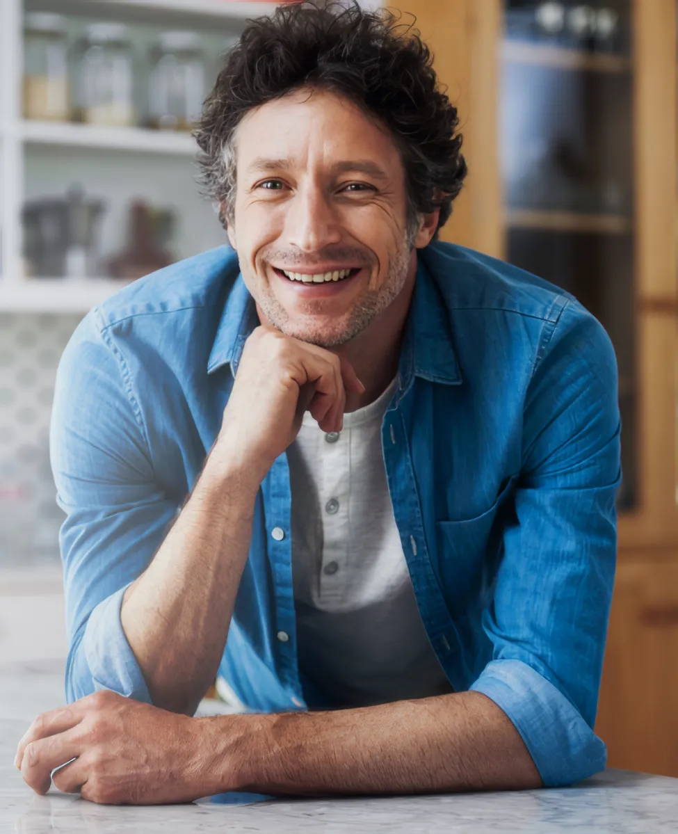 smiling man leans on kitchen countertop at home utc
