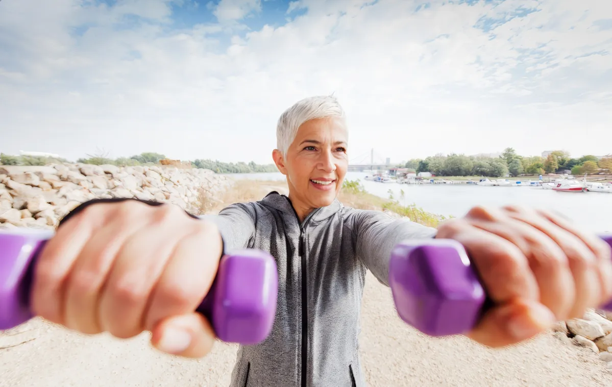woman exercising outdoors with purple hand weights utc