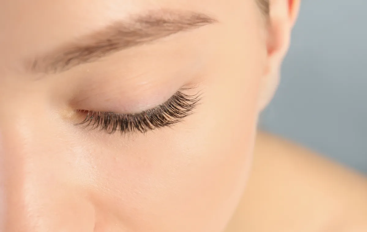 young woman with beautiful long eyelashes on gray utc